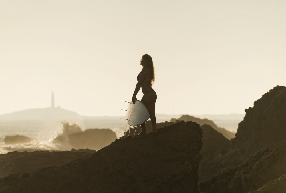 Silhouette of a female surfer holding her surfboard while standing on a rock at the coast andalusia spain Canvas Art - Ben Welsh Design Pics (36 x 24)
