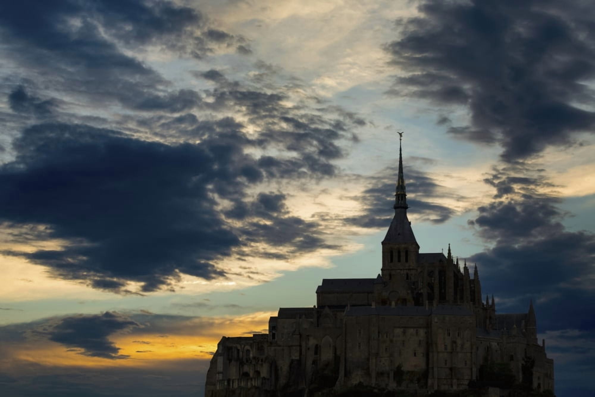 Silhouette of large stone Abbey perched on rocky hill with dramatic clouds at sunset Mont St Michel Brittany France Canvas Art - Michael Interisano Design Pics (19 x 12)