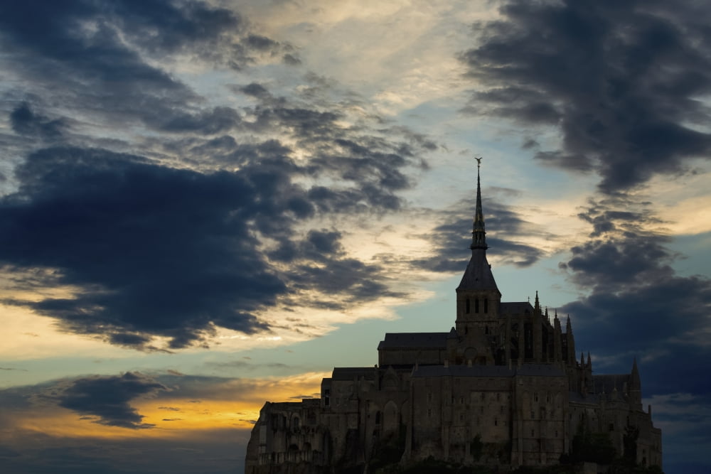 Silhouette of large stone Abbey perched on rocky hill with dramatic clouds at sunset Mont St Michel Brittany France Canvas Art - Michael Interisano Design Pics (38 x 24)