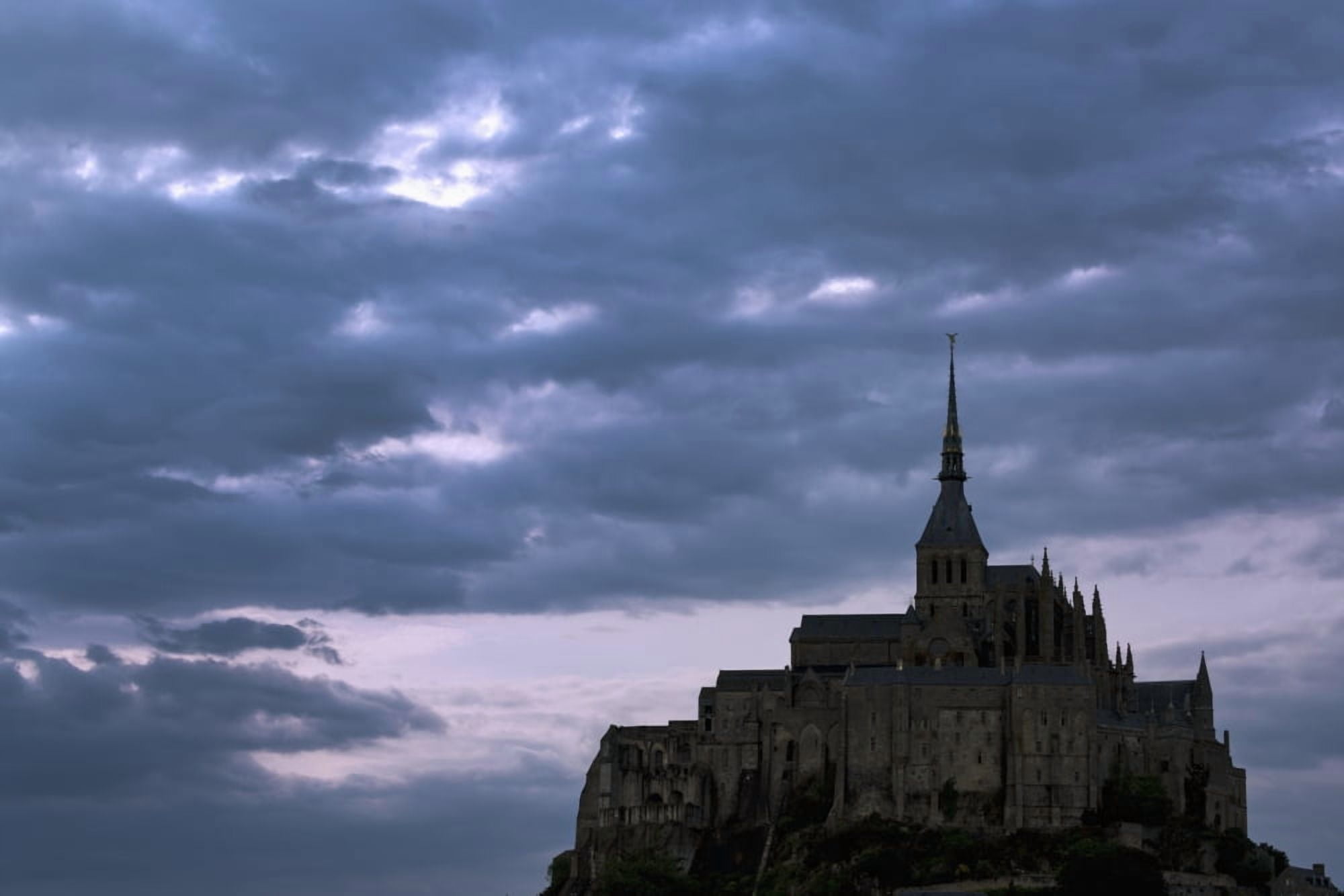 Silhouette of large stone Abbey perched on rocky hill with dramatic clouds at sunset Mont St Michel Brittany France Canvas Art - Michael Interisano Design Pics (38 x 24)