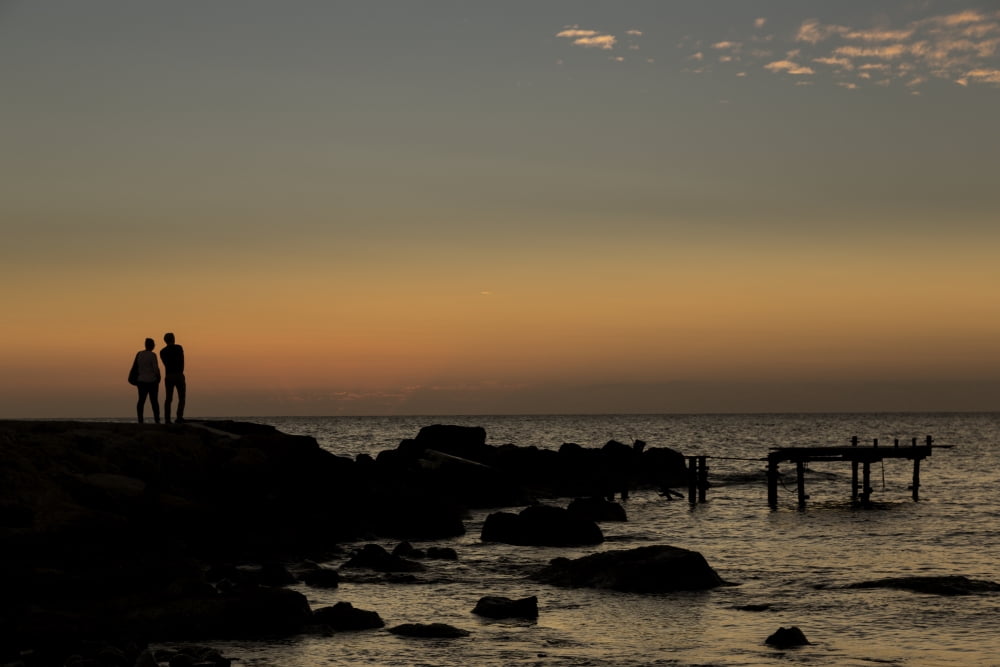 Silhouette of two people standing at the waters edge watching the sunset over the water Paphos Cyprus Canvas Art - John Short Design Pics (38 x 24)