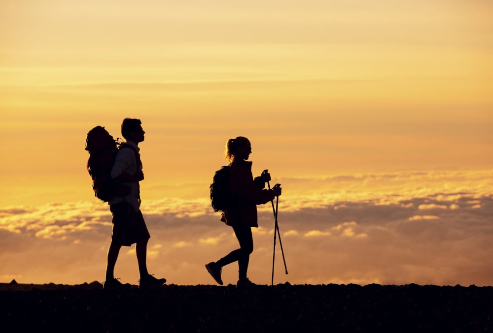 Silhouettes of two hikers with backpacks walking at sunset Trekking and enjoying the sunset view from mountain top above the clouds Canvas Art - Design Pics Vibe Design Pics (16 x 11)