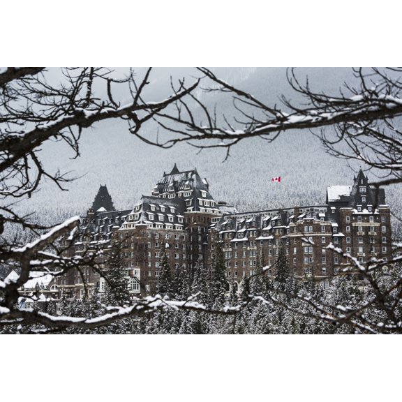 Snow covered Banff Springs Hotel framed by tree limbs with snow covered trees on mountain hillside in the background Banff Alberta Canada Canvas Art - Michael Interisano Design Pics (19 x 12)