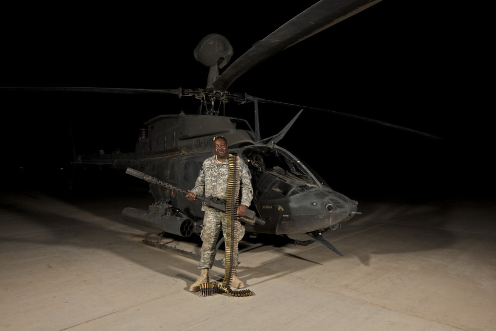 Soldier holding a 50 caliber machine gun in front of an OH-58D Kiowa Warrior Canvas Art - Terry MooreStocktrek Images (35 x 23)