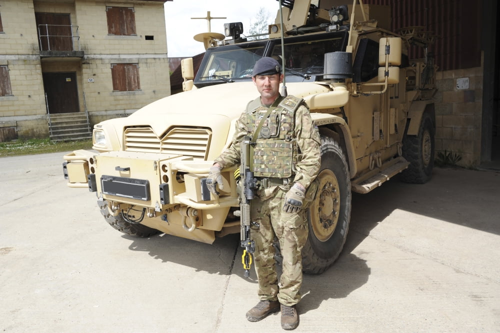 Soldier standing in front of a Husky TSV armored vehicle of the British Army Canvas Art - Andrew ChittockStocktrek Images (34 x 23)