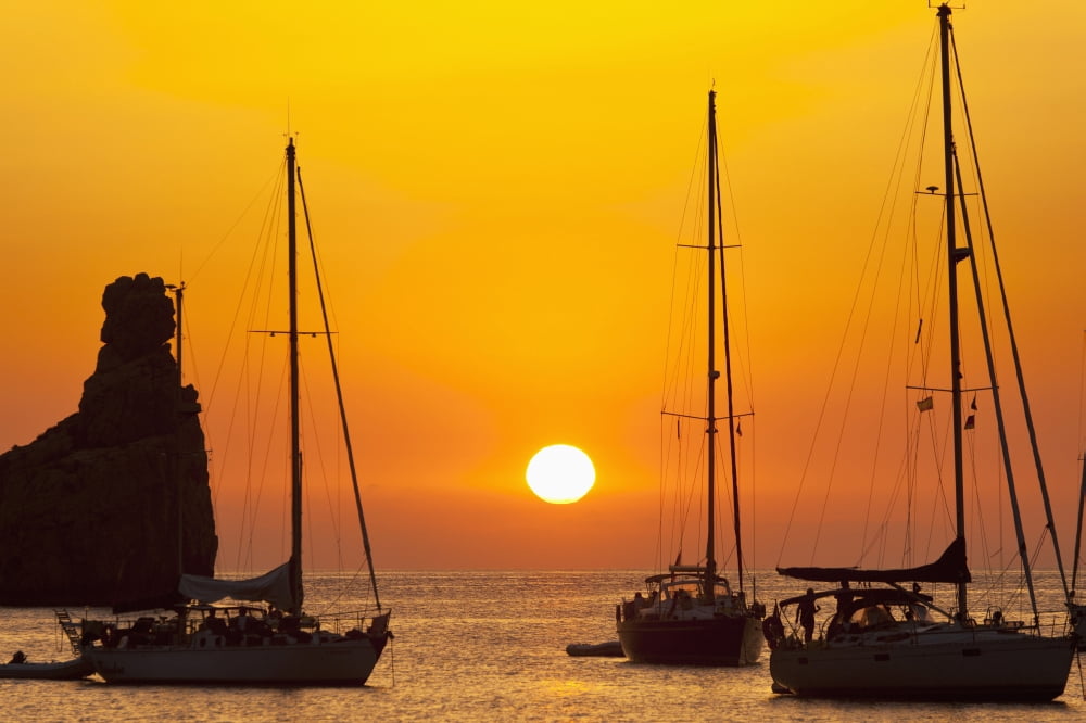 Spain Yachts and strange shaped rock off Benirras beach at dusk Ibiza Canvas Art - Ian Cumming Design Pics (19 x 12)