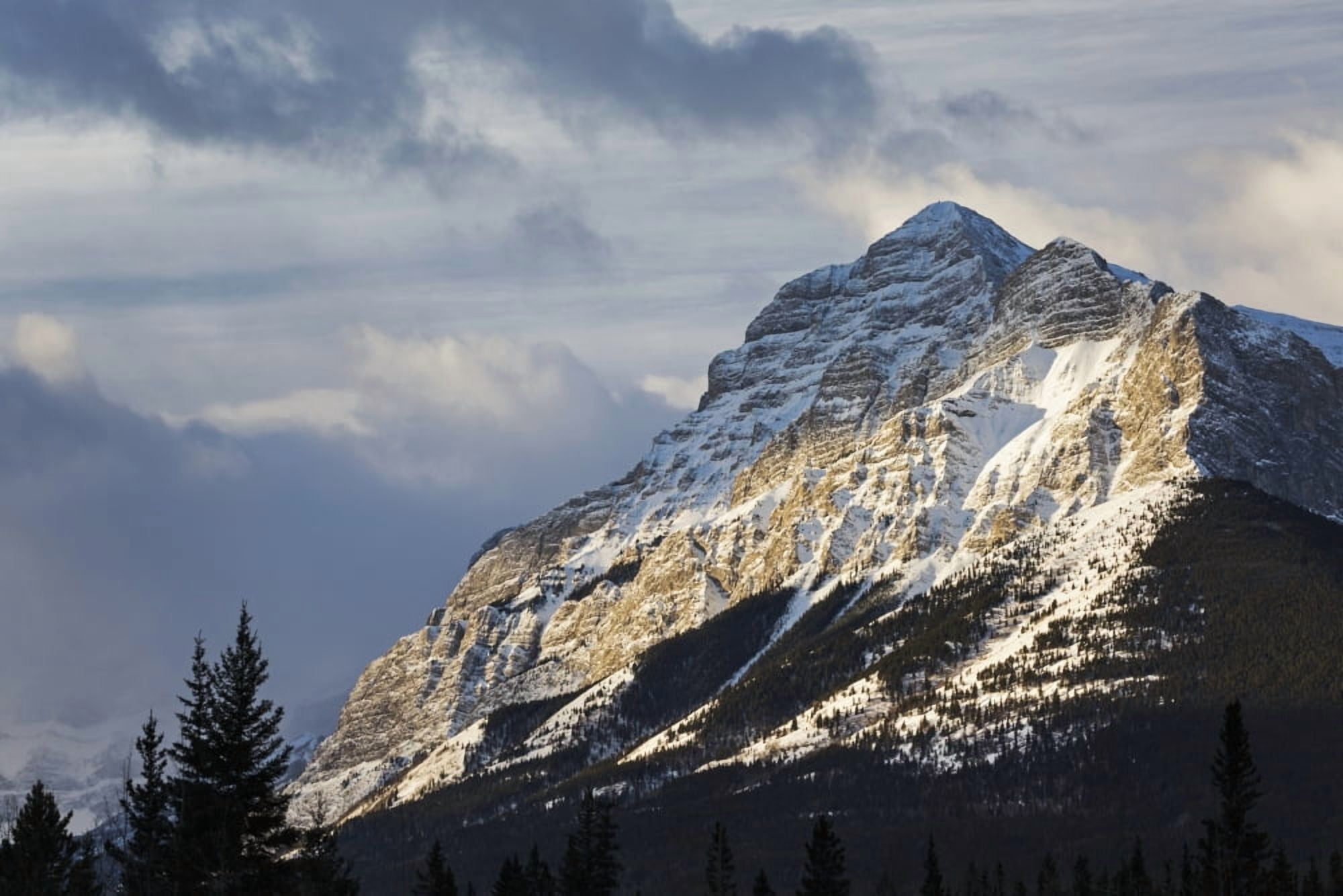 Sun breaking through the clouds partially lighting a snow covered mountain with clouds in the sky Kananaskis Country Alberta Canada Canvas Art - Michael Interisano Design Pics (19 x 12)