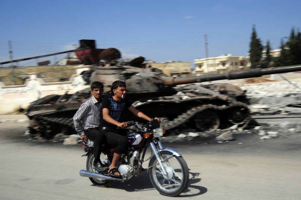 Syrian men drive a motorbike past a destroyed T-72 battle tank Canvas Art - Andrew ChittockStocktrek Images (18 x 12)