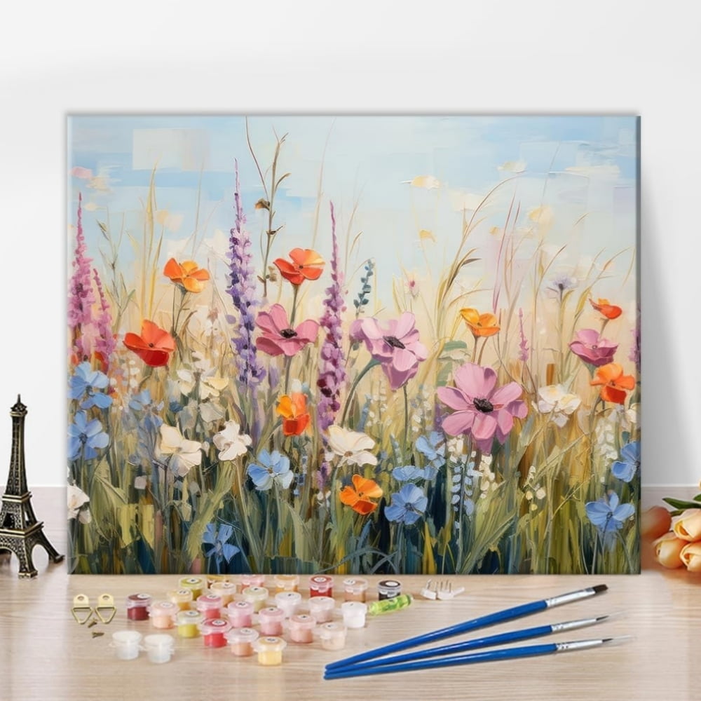 A painting of flowers in a field with paint and three paintbrushes in front of it