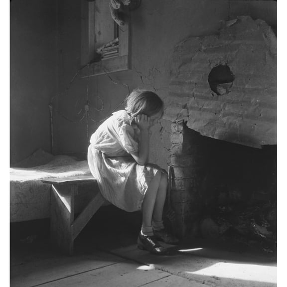 The Great Depression. Young Girl Sitting On Bench Near Fireplace With Bed In Background In A Taos History