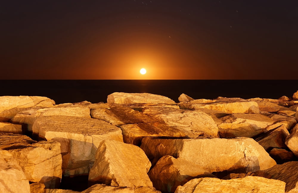 The moon rising behind rocks lit by a nearby fire in Miramar Argentina Canvas Art - Luis ArgerichStocktrek Images (35 x 23)