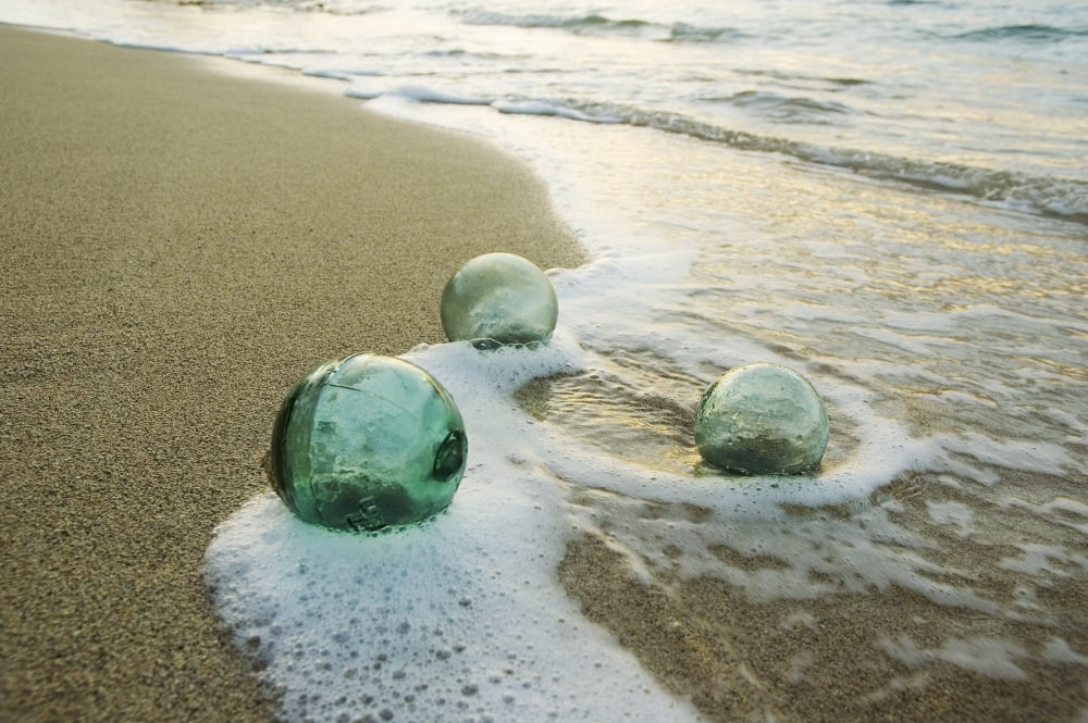 Three Glass Fishing Floats Roll On The Sandy Shoreline With Ripples Of Water And Seafoam Canvas Art - Mary Van de Ven  Design Pics (34 x 22)