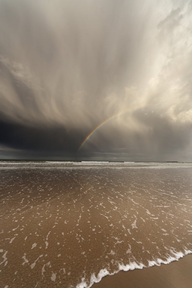 Tide Coming Up Onto The Beach With A Rainbow In The Clouds Bamburgh England Canvas Art - John Short Design Pics (12 x 19)