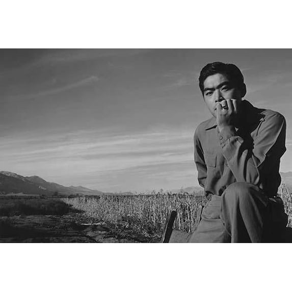 Tom Kobayashi, half-length portrait, seated in a field, his elbow resting on his knee and his hand on his chin, facing front. Ansel Easton