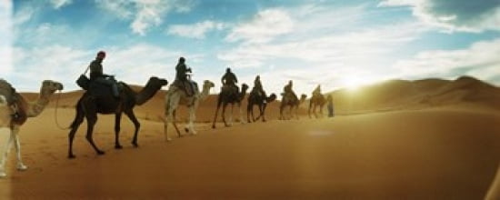 Tourists riding camels through the Sahara Desert landscape led by a Berber man Morocco Canvas Art - Panoramic Images (30 x 12)