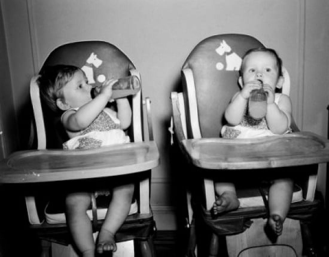 Two babies sitting in high chairs drinking from baby bottles Canvas Art - (18 x 24)