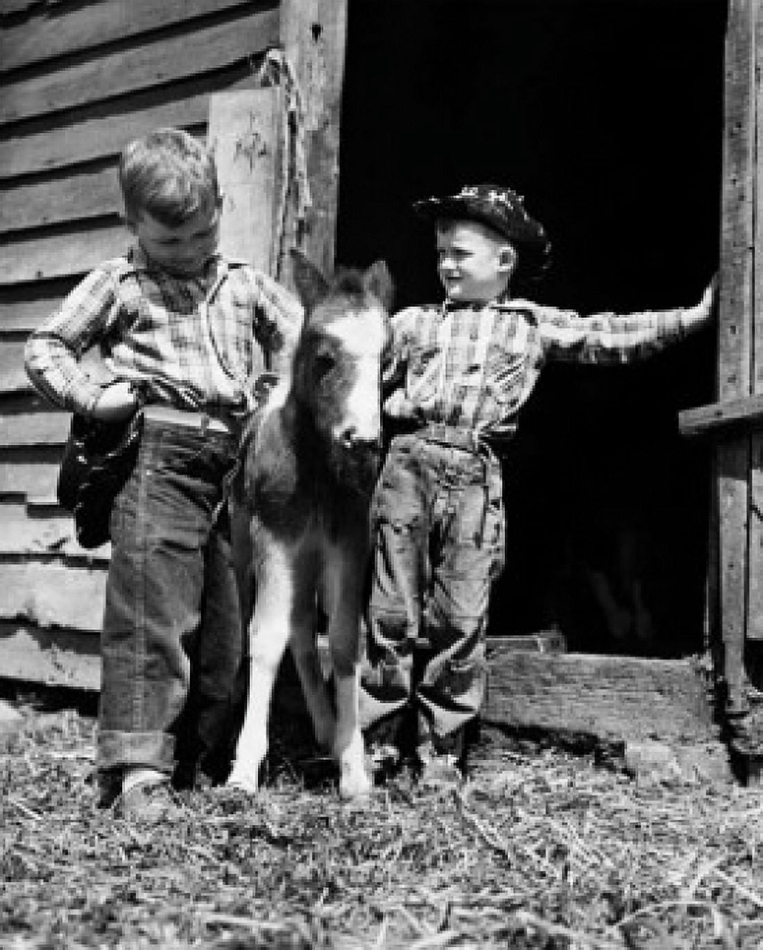 Two cowboys standing with a foal in front a stable Canvas Art - (24 x 36)