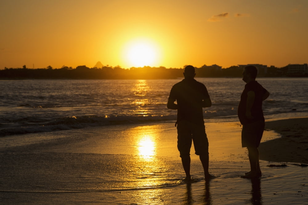 Two men stand in the tide water on a beach at sunset Caloundra Queensland Australia Canvas Art - John Short Design Pics (19 x 12)