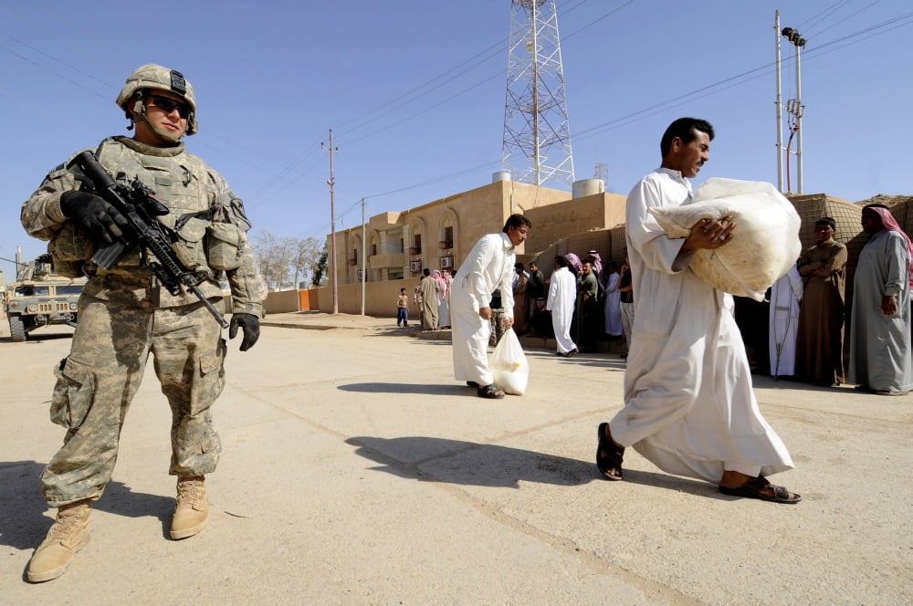 US Army soldier stands guard as locals walk away with food supplies Canvas Art - Stocktrek Images (34 x 23)