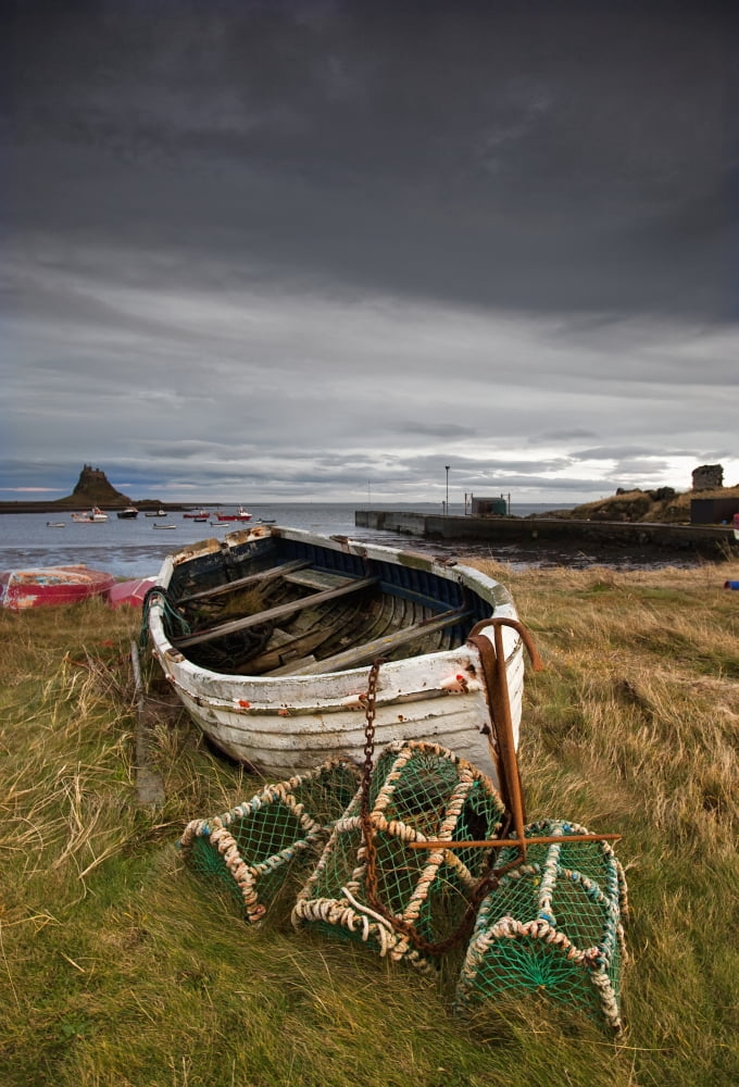 A Weathered Boat And Fishing Equipment Sitting On The Shore With Lindisfarne Castle In The Distance Lindisfarne Northumberland England Canvas Art - John Short Design Pics (24 x 36)