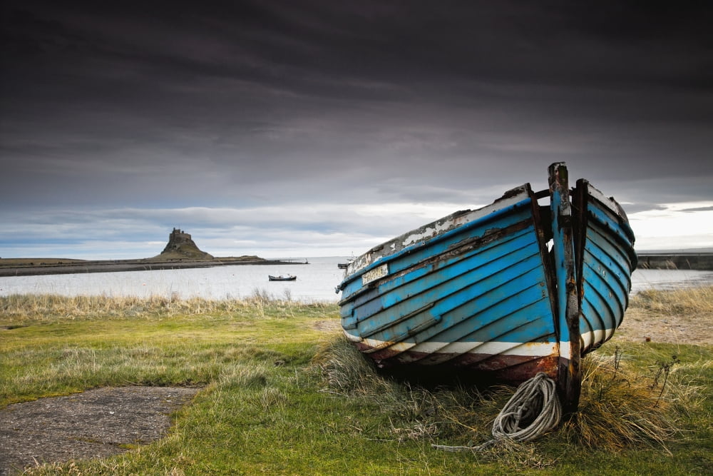 A Weathered Boat Sitting On The Shore With Lindisfarne Castle In The Distance Lindisfarne Northumberland England Canvas Art - John Short Design Pics (38 x 24)