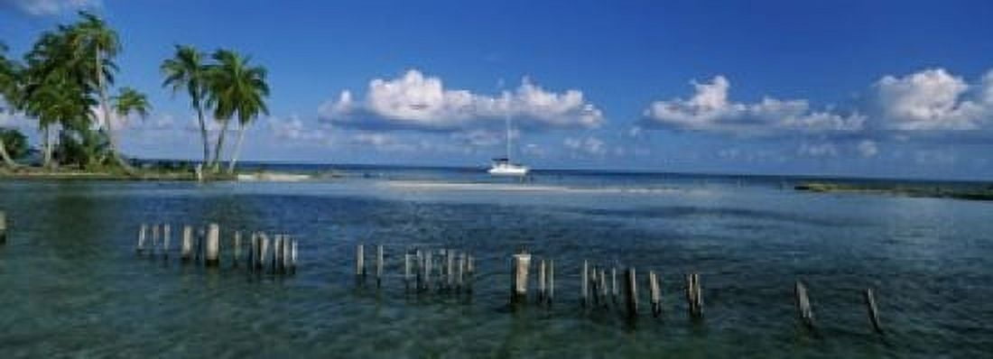 Wooden posts in the sea with a boat in background Laughing Bird Caye Victoria Channel Belize Canvas Art - Panoramic Images (18 x 7)
