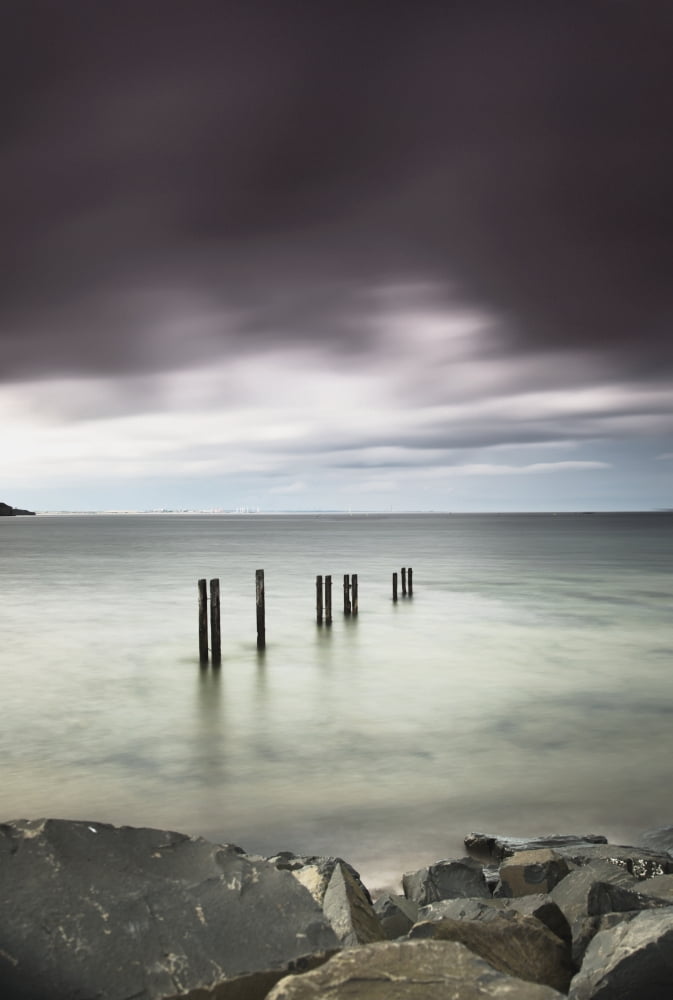 Wooden posts in a row in the shallow water along the coast under dark storm cloudsSt marys bay northumberland england Canvas Art - John Short Design Pics (12 x 18)