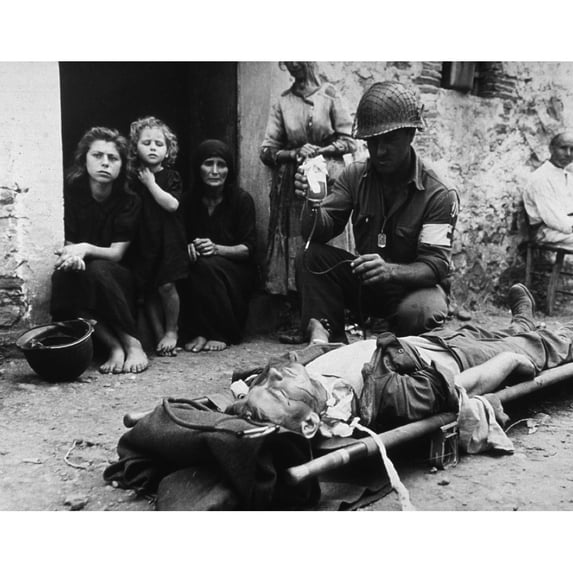 Wounded U.S. Soldier Receives Blood Plasma While Lying On A Stretcher In A Street In Sicily During World War Ii. Behind