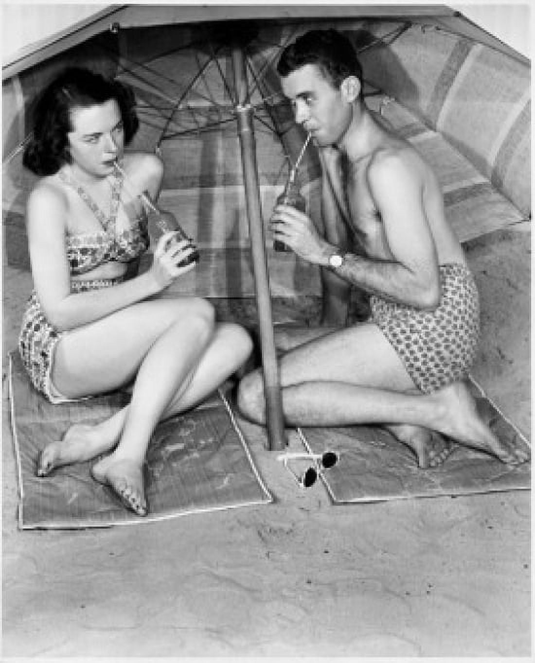 Young couple sitting under beach umbrella drinking Canvas Art - (18 x 24)