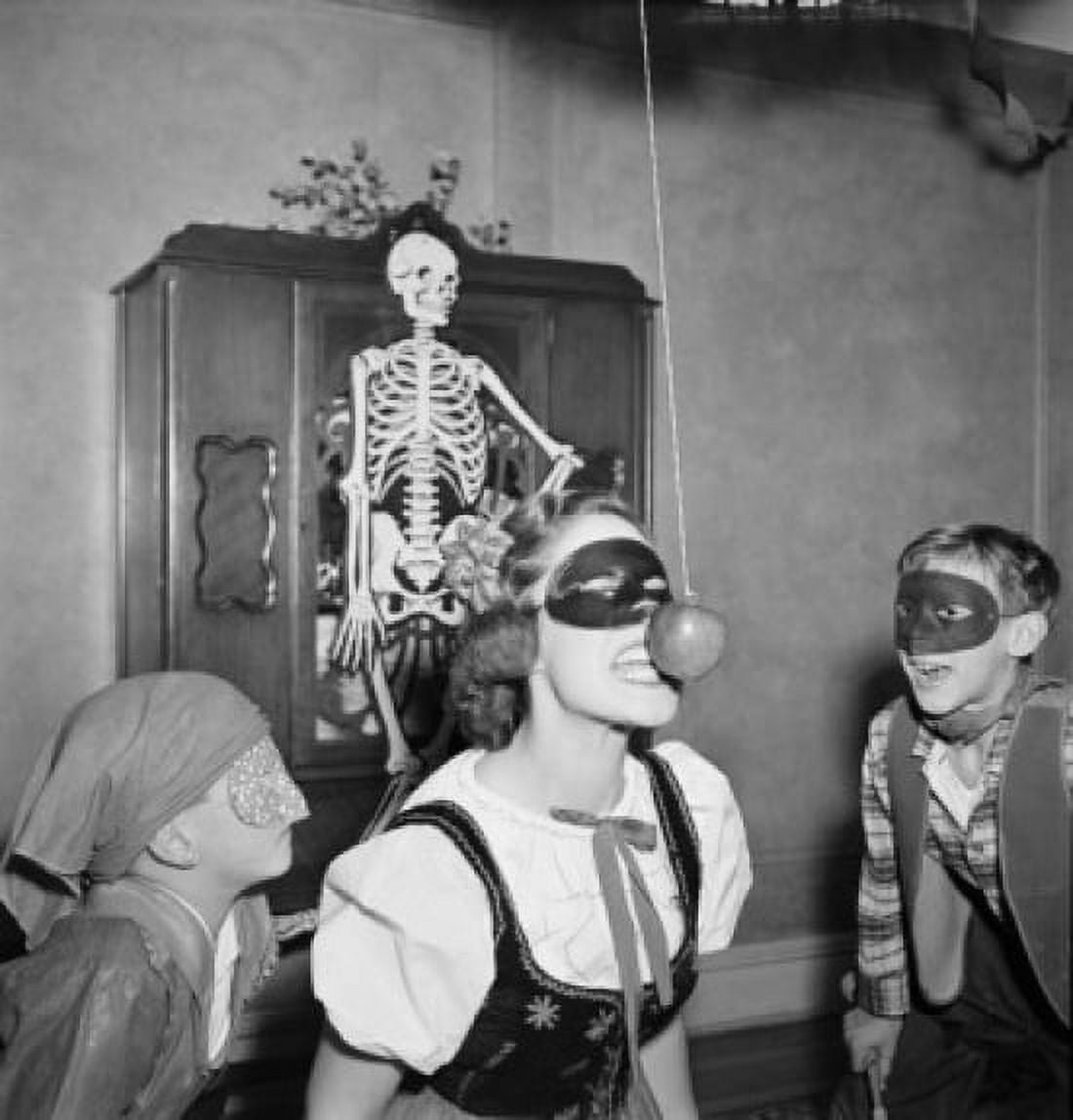 Young woman attempting to bite apple while two boys are watching during Halloween Canvas Art - (24 x 36)