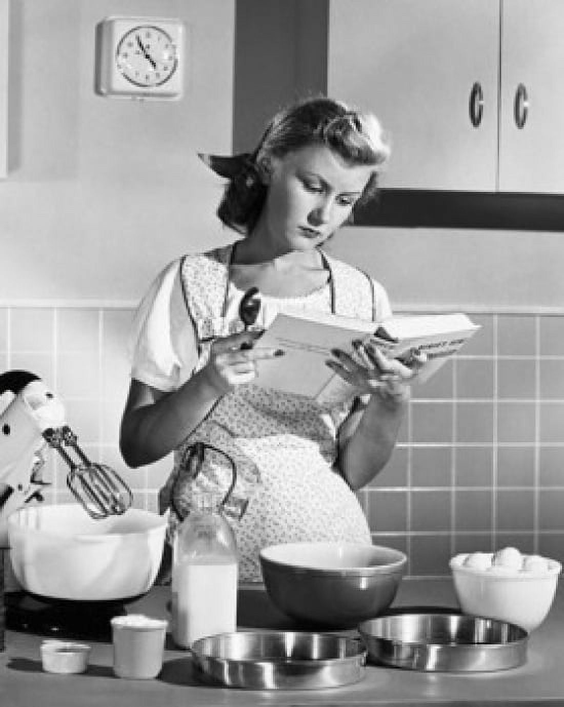 Young woman reading a cookbook in a domestic kitchen Canvas Art - (24 x 36)