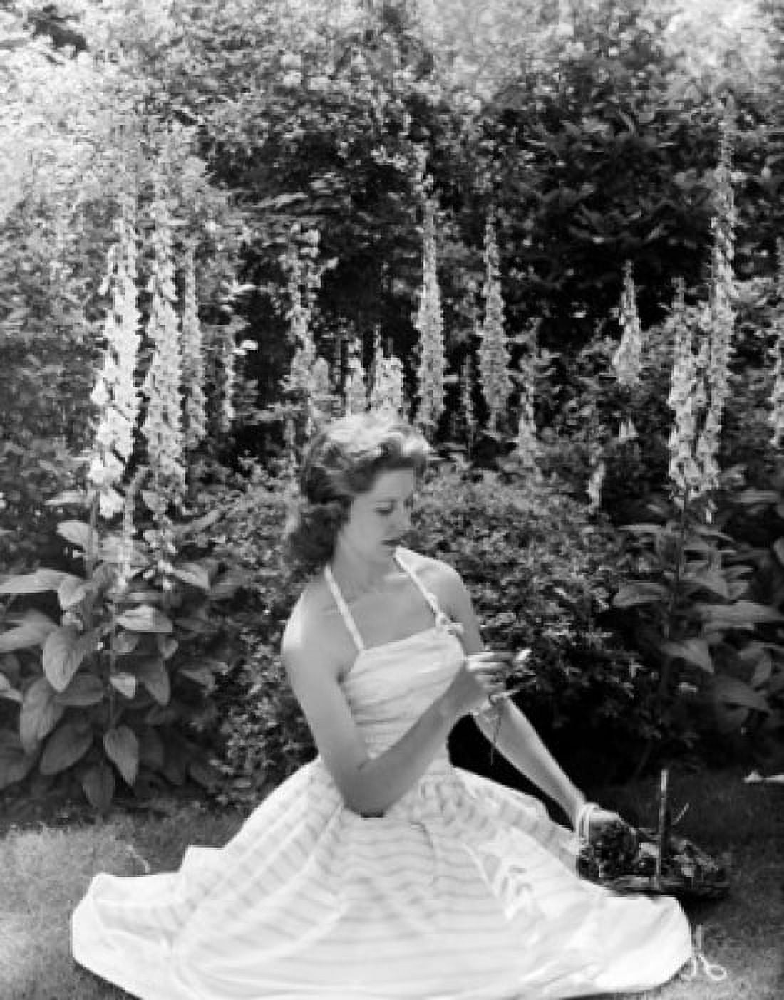 Young woman sitting in garden and holding flower Canvas Art - (18 x 24)