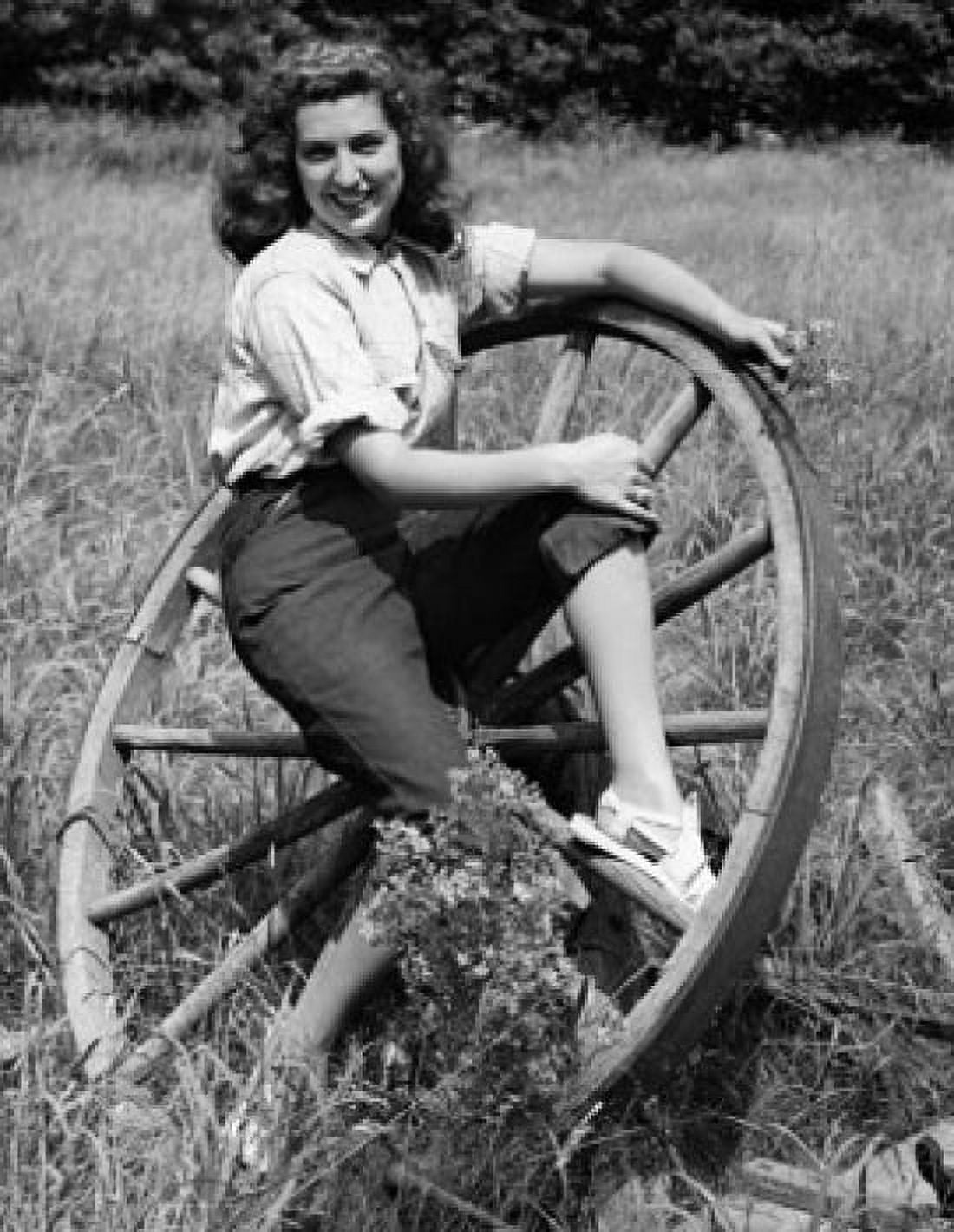 Young woman sitting on a wagon wheel and smiling Canvas Art - (18 x 24)