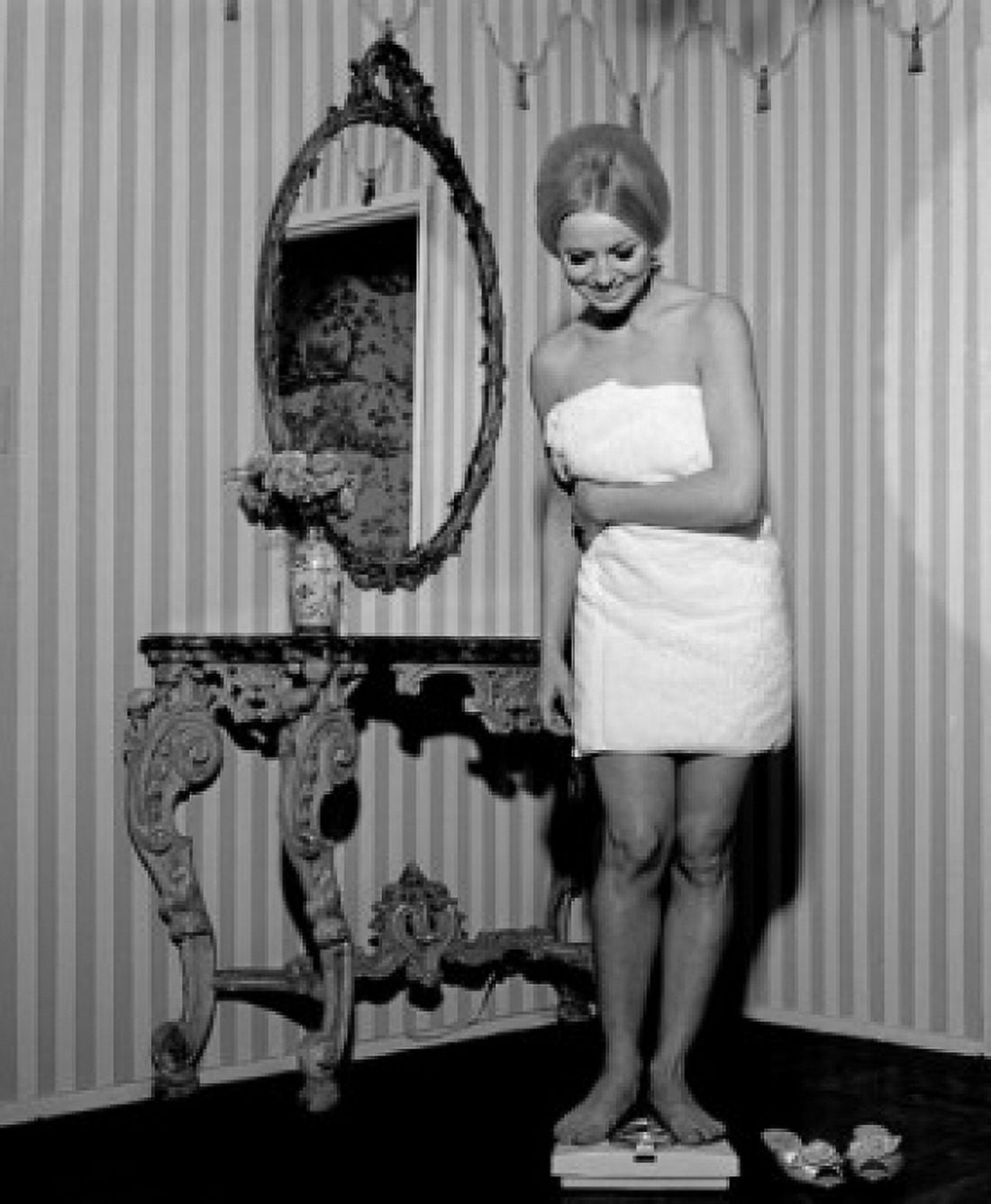 Young woman wrapped in towel standing on weight scale and smiling Canvas Art - (24 x 36)