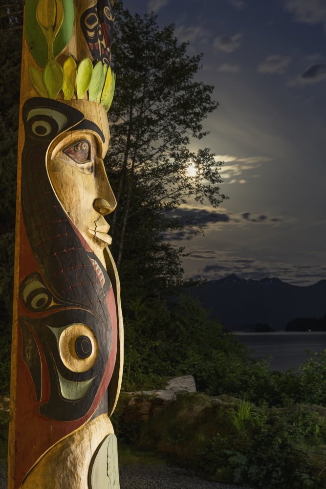A large totem pole lit up at night in Sitka National Historic Park with the moon and clouds in the background Sitka Alaska United States of America Canvas Art - Kevin Smith Design Pics (24 x 38)