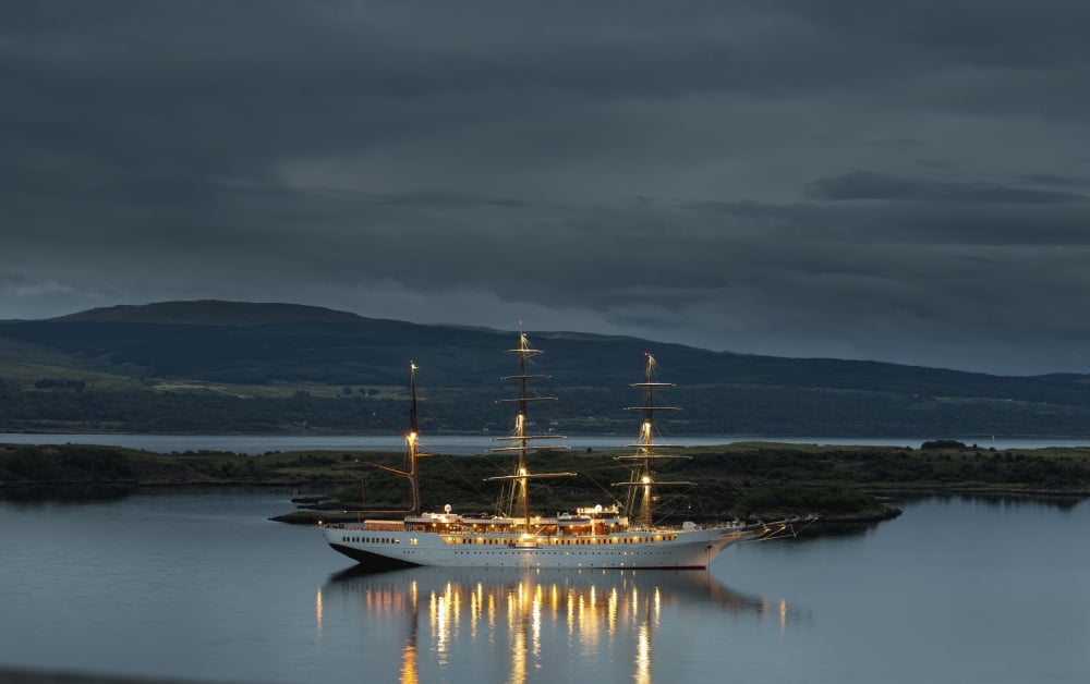 A large white boat with masts illuminated on the tranquil water along the coast at dusk Tobermory Isle of Mull Argyll and Bute Scotland Canvas Art - John Short  Design Pics (38 x 24)
