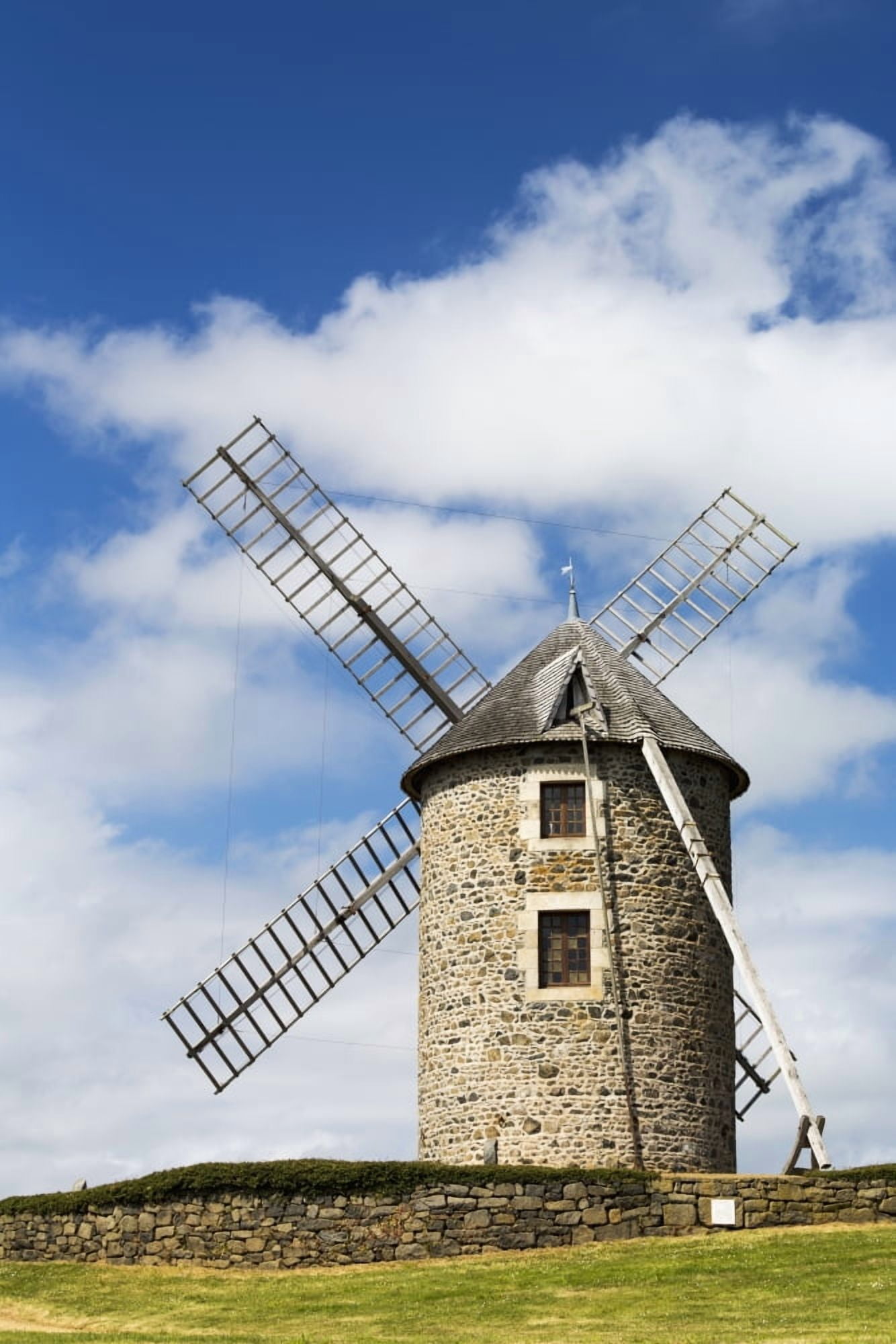 An old stone windmill on a hillside with wooden blades surrounded by a stone fence with blue sky and clouds Brehec Brittany France Canvas Art - Michael Interisano Design Pics (12 x 19)