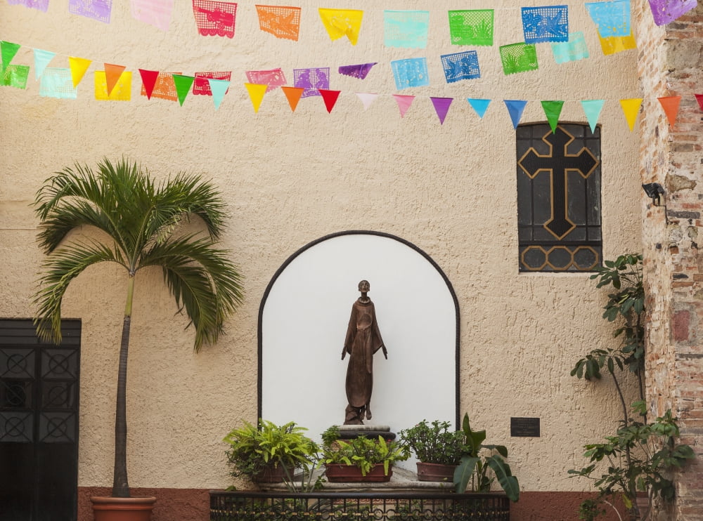 A sculpture of san francisco de assisi is sheltered by the church of our lady of guadalupePuerto vallarta mexico Canvas Art - Debra Brash Design Pics (18 x 13)