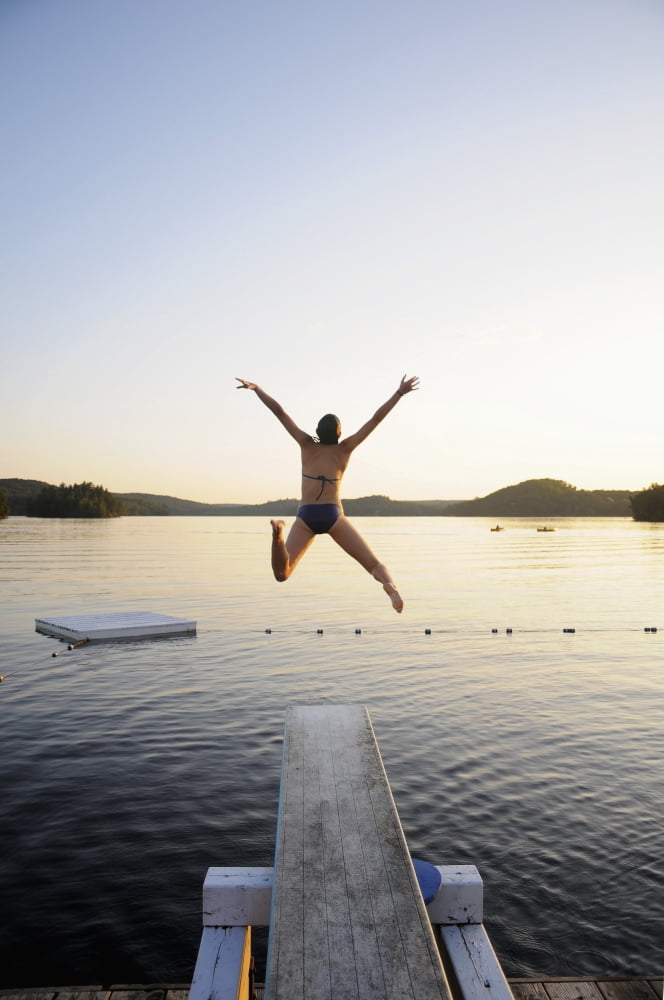 A swimmer jumps off a diving board as the sun sets over a lake in Muskoka Huntsville Ontario Canada Canvas Art - James MacDonald Design Pics (12 x 19)